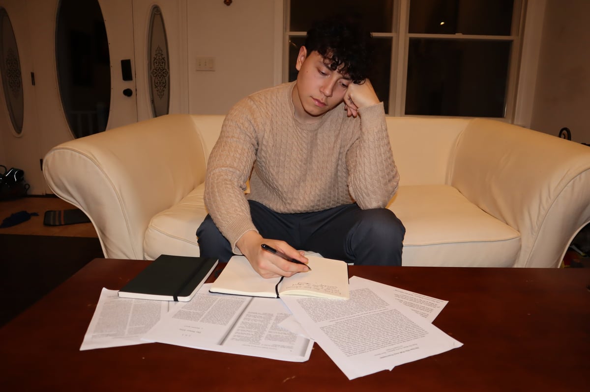 Man sitting on a cream-colored couch reviewing documents spread on a table in front of him